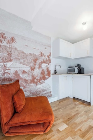 Eine moderne Küche mit weißen Schränken und einer Mikrowelle, einem Holzboden und einem leuchtend orangefarbenen Sofa mit Kissen.