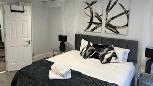 A modern bedroom with a large bed, a bedside table, a nightstand, and abstract wall art. - Tavistock House-parking-sleeps 7-central (Bedford)