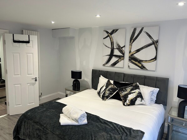A modern bedroom with a large bed, a bedside table, a nightstand, and abstract wall art. - Tavistock House-parking-sleeps 7-central (Bedford)