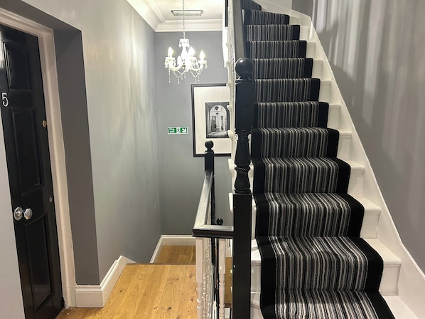 A staircase with black and white striped carpet, a chandelier, and a fire exit sign. - Tavistock House-parking-sleeps 7-central (Bedford)