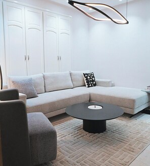 A modern living room with a sectional sofa, a round coffee table, and a hanging light fixture. - Al Anbar 8-2 Apartment - Your Cozy Retreat in the Heart of Sfax Chez-moi (Sfax)