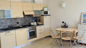 Une cuisine compacte dotée d’appareils électroménagers modernes, un coin repas avec une table ronde et des chaises, et un tableau encadré au mur.