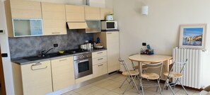 Une cuisine compacte dotée d’appareils électroménagers modernes, un coin repas avec une table ronde et des chaises, et un tableau encadré au mur.