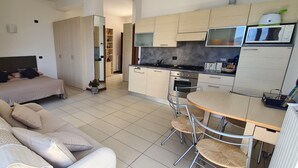 Ein kleines Hotelzimmer mit Bett, Sofa, Esstisch, Stühlen, Küchenzeile und einem großen Spiegel.