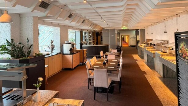 A modern hotel lobby with a long reception desk, seating area, and a kitchen visible in the background. - Roomie Hotel (Schriesheim)