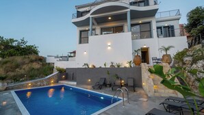 Una casa moderna de dos pisos con piscina, mobiliario exterior y un muro de piedra.
