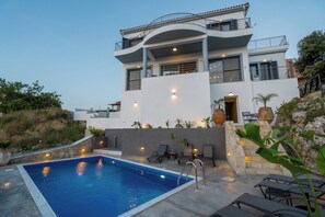 Ein modernes, zweistöckiges Haus mit Swimmingpool, Sitzgelegenheiten im Freien und einer Steinmauer.