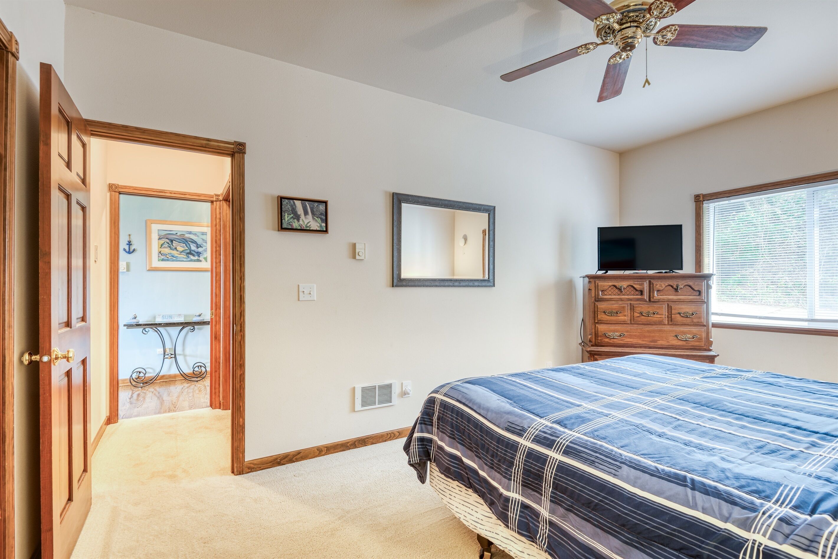 Une chambre à coucher comprenant un lit, une commode, un téléviseur, un ventilateur de plafond et une fenêtre.