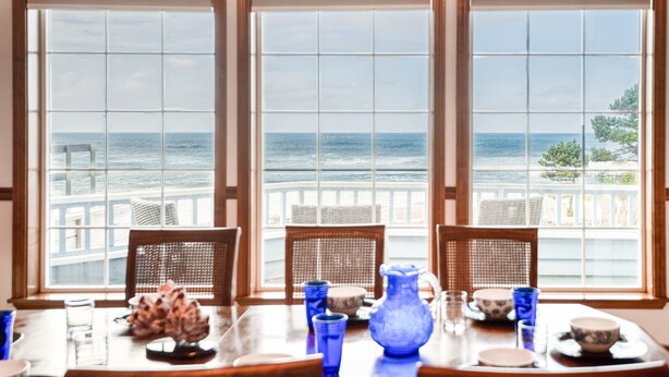 Een eettafel met stoelen en uitzicht op de oceaan door grote ramen.
