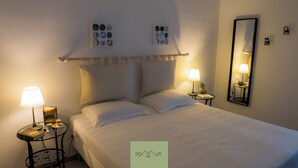 Un lit bien fait, avec du linge de lit blanc, deux tables de chevet avec des lampes, un miroir et des œuvres d’art accrochées au mur.