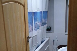 Une salle de bain avec une porte en bois, un mur recouvert de carreaux blancs et une affiche représentant un paysage urbain.
