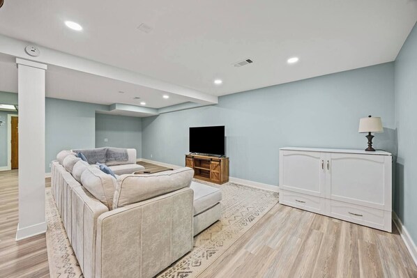 A modern living room with a sectional sofa, a flat-screen TV, a cabinet, and a lamp.