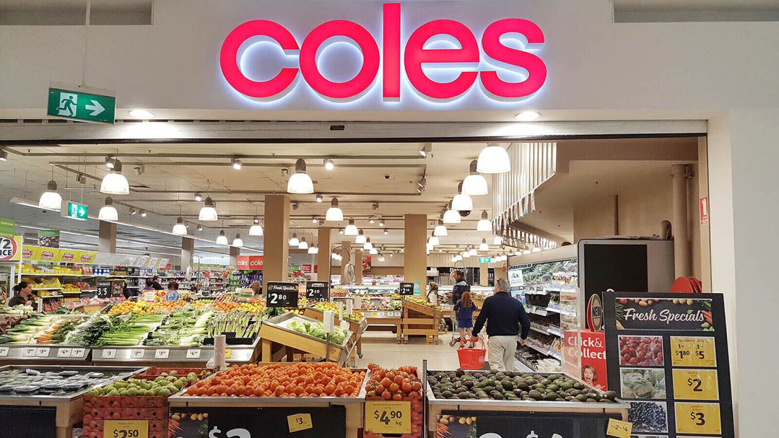 Interieur van een supermarkt met een opvallend 'Coles'-bord, verschillende afdelingen met vers fruit en groenten, en zichtbare prijskaartjes.
