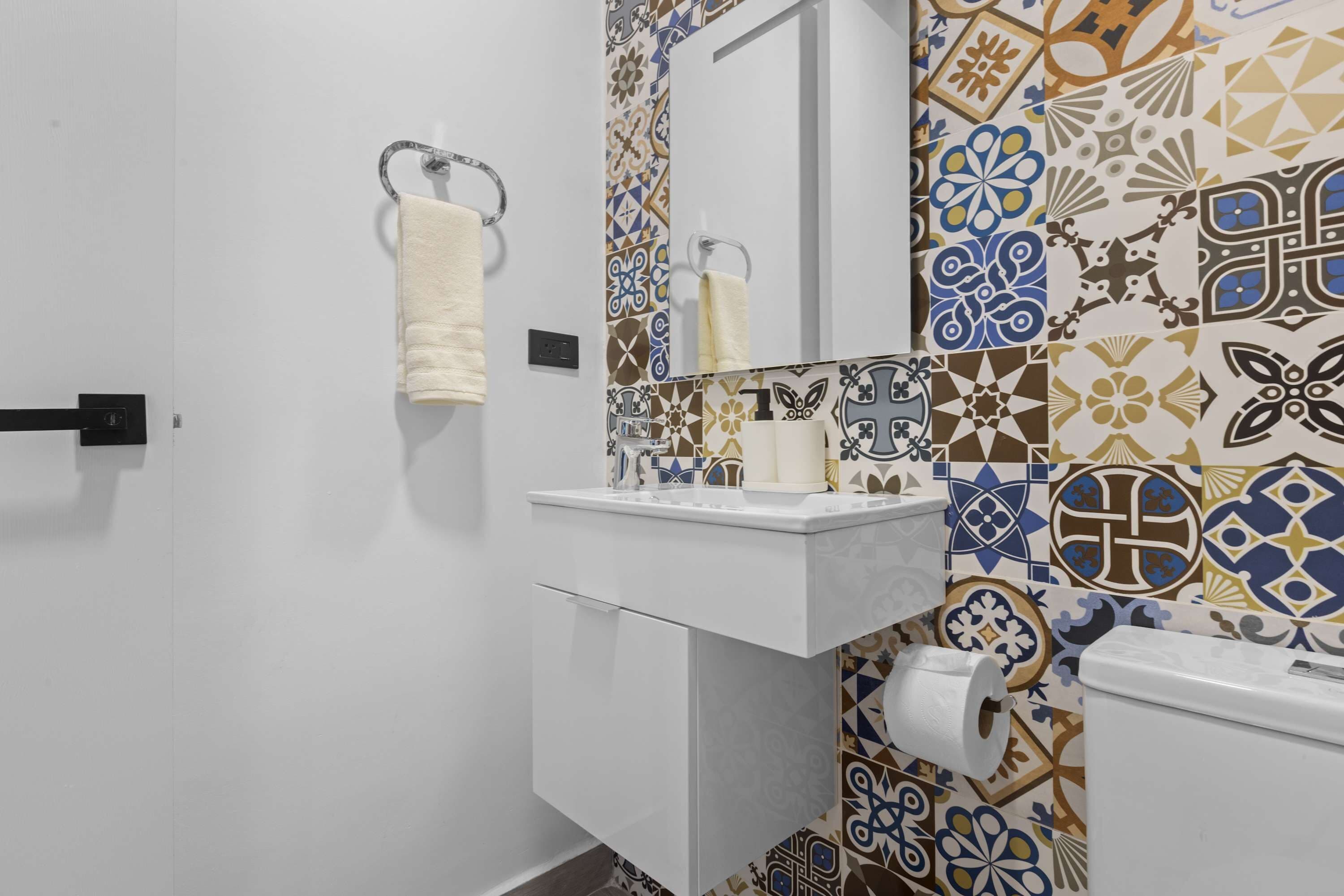 A bathroom with a white sink, a mirror, and patterned tiles on the walls.