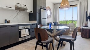 A modern kitchen with a dining area, featuring a round glass table, dark chairs, and a large window with a view. - NOK Cozy 1BR Apartment the Towers By Vistacana (Punta Cana)