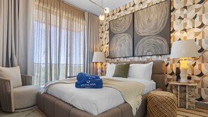 A modern hotel room with a large bed, two side tables with lamps, a view of the outdoors, and abstract wall art. - NOK Cozy 1BR Apartment the Towers By Vistacana (Punta Cana)