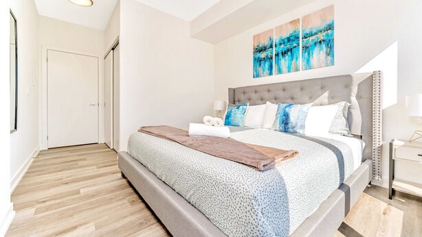 A modern bedroom with a large bed, a tufted headboard, and abstract wall art. - High Rise 1BR Building With Gorgeous Views (Kitchener)