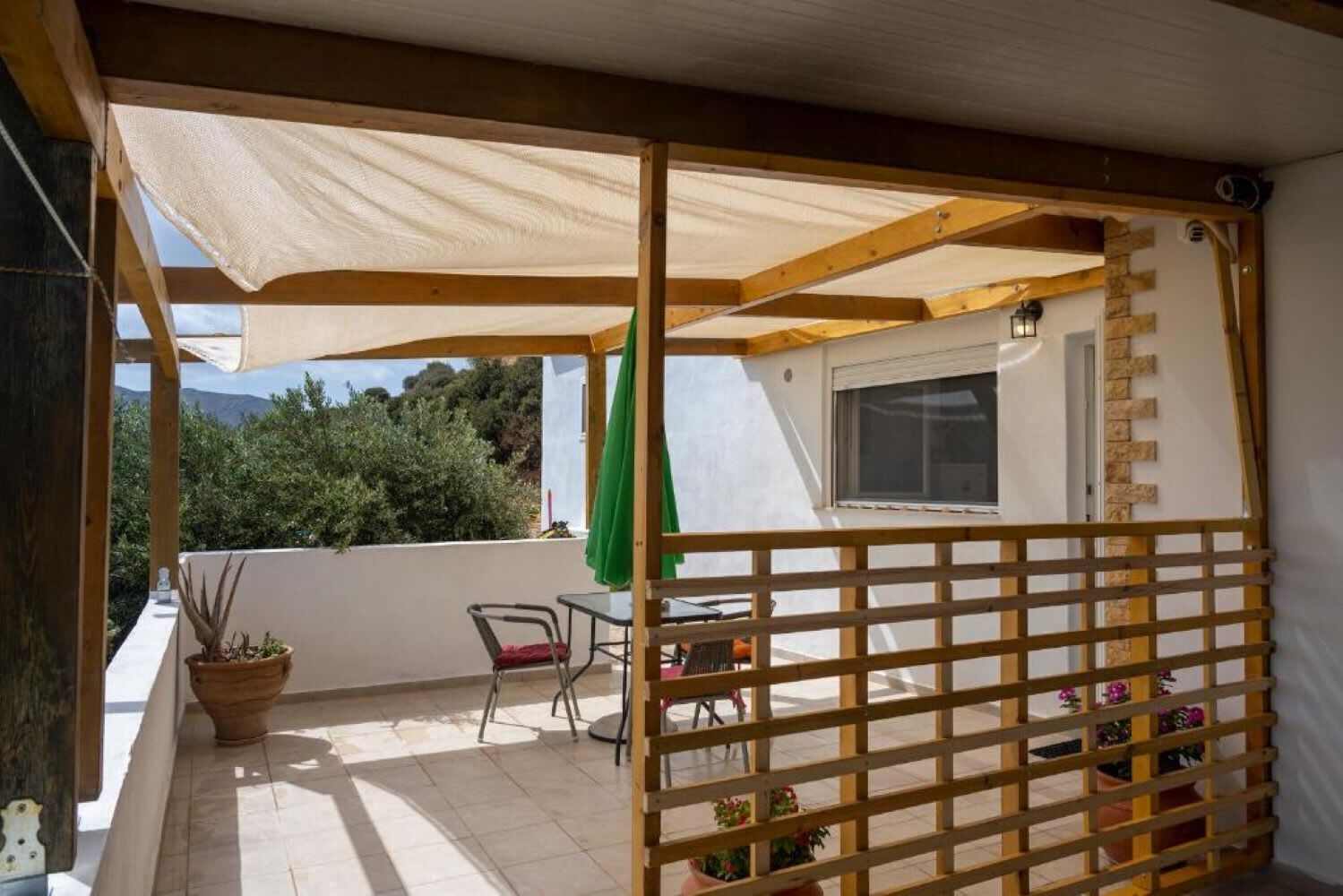 Un espacio al aire libre techado con un porche de madera, una mesa con sillas y plantas en macetas.