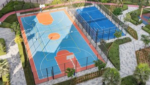 A basketball court with a surrounding fence, palm trees, and a tiled walkway. - Stayshort - 1 Bed in JGC Sleeps 4 With Balcony (Dubai)