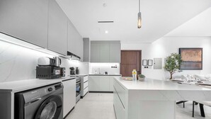 A modern kitchen with a built-in washer, a large island, and a dining area. - Stayshort - 1 Bed in JGC Sleeps 4 With Balcony (Dubai)