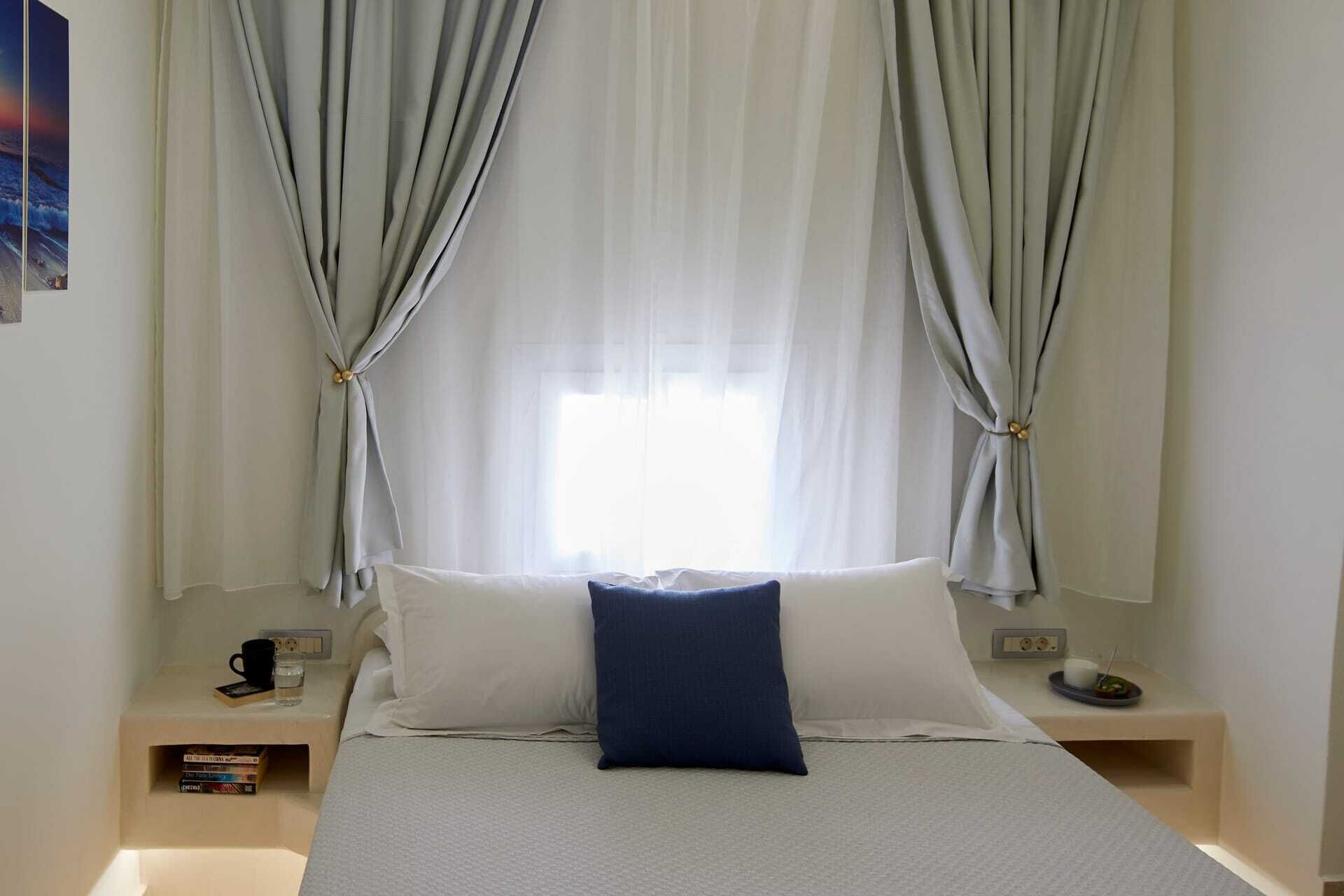 A bedroom with a bed, two nightstands, a window with curtains, and a wall-mounted picture.