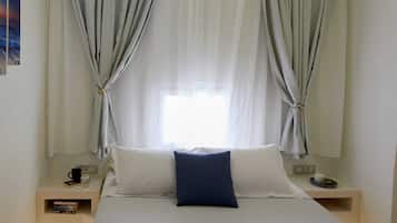 A bedroom with a bed, two nightstands, a window with curtains, and a wall-mounted picture.