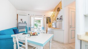 Ein heller, freundlicher Raum mit einem weißen Tisch und einem blauen Sofa, einer Treppe mit gelber Geländer und einer Tür mit blauem Rahmen.