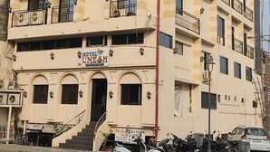 Ein mehrstöckiges Hotel mit Balkonen, einem Hinweisschild, das es als Hotel kennzeichnet, und einigen geparkten Fahrzeugen davor.