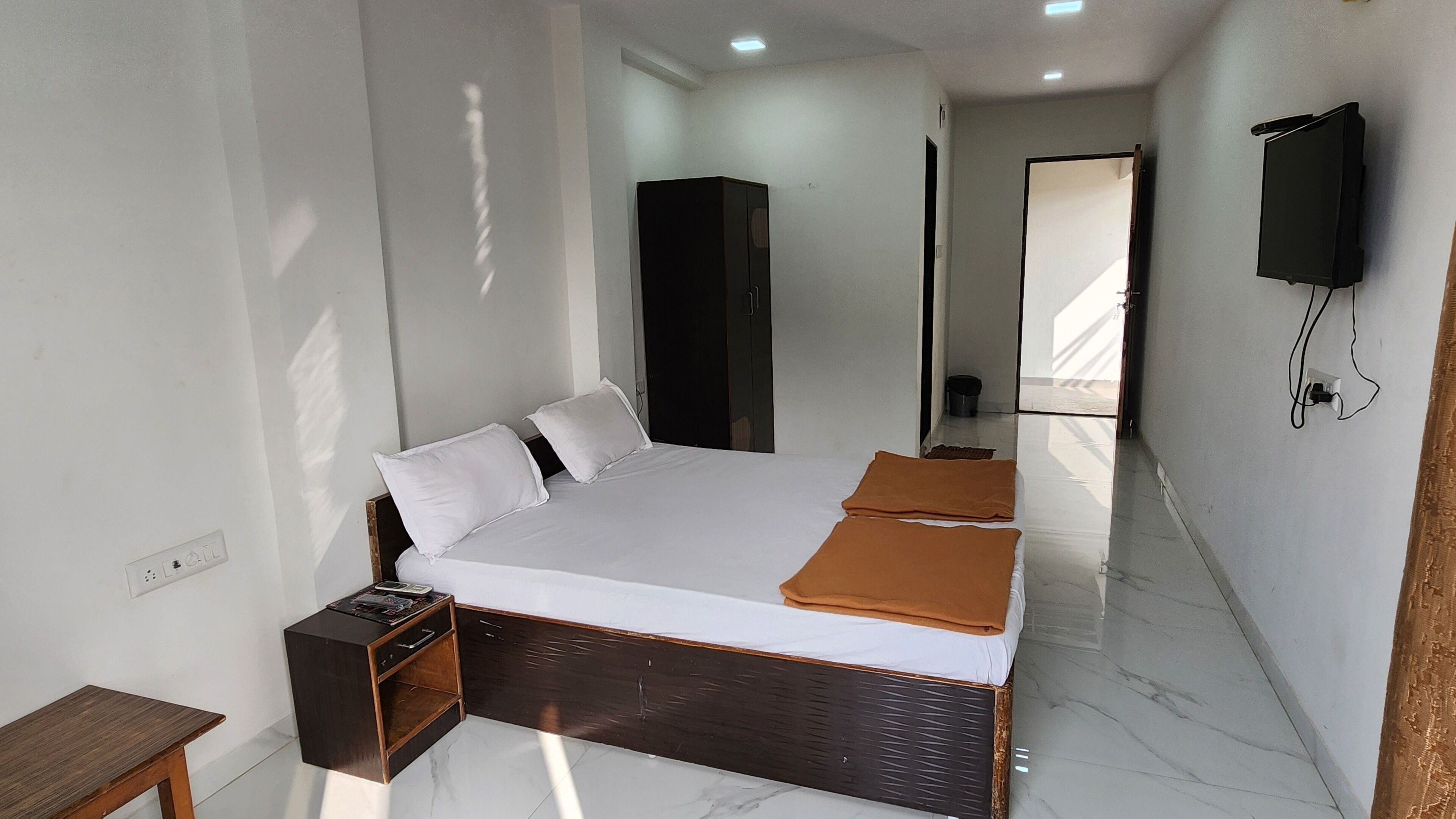 Una habitación de hotel moderna con una cama grande, una mesita de noche, un armario, un televisor montado en la pared y un baño visible a través de una puerta abierta.