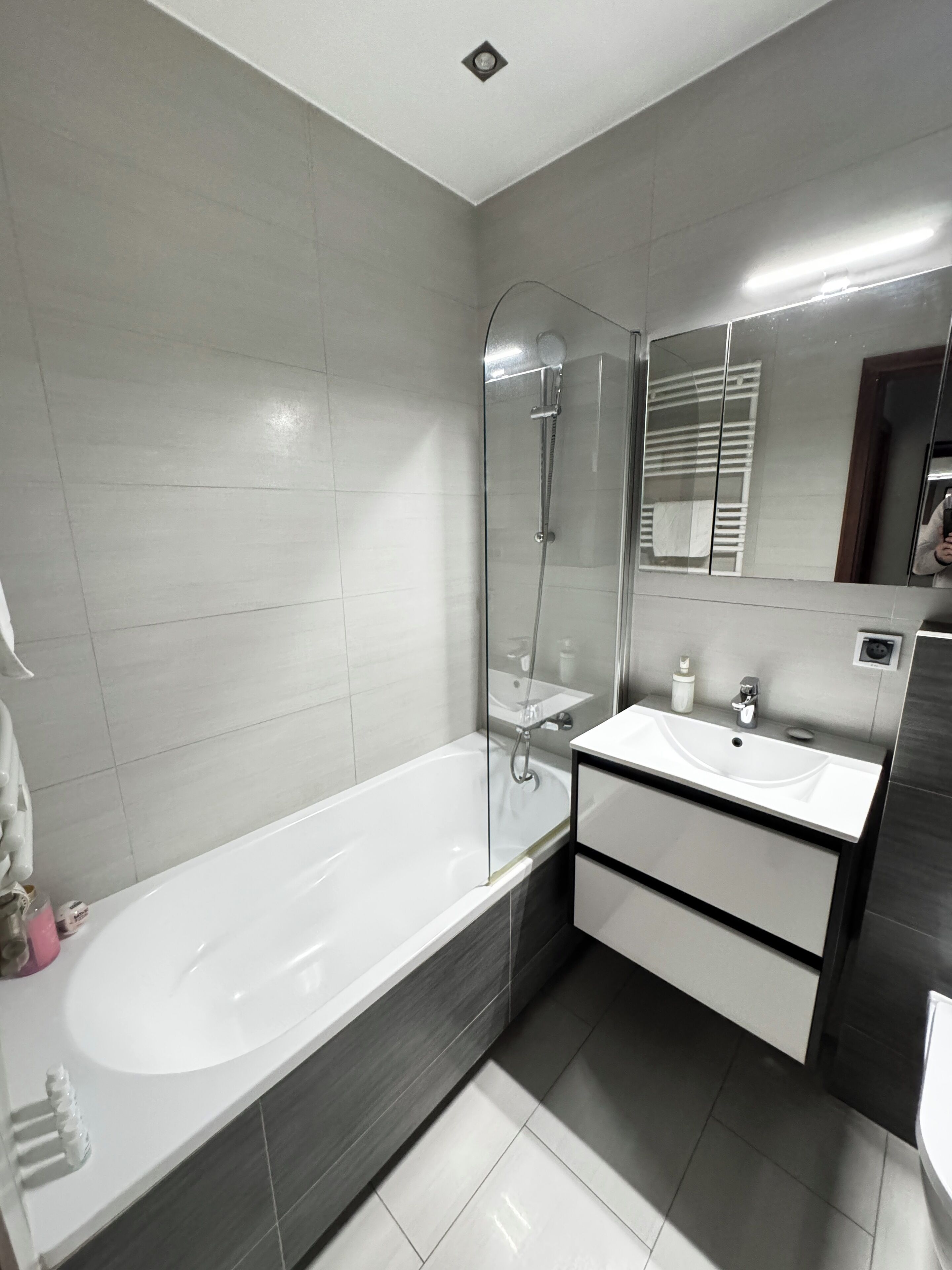 A modern bathroom with a glass-enclosed shower, a white bathtub, and a vanity with a sink and mirror.