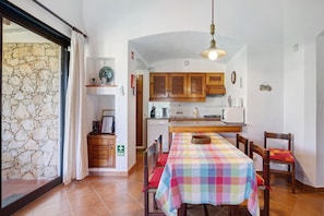 A kitchen with wooden cabinets, a dining table with a checkered tablecloth, and a stone wall. - Lotus villa 2, albufeira (Albufeira)