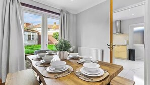 A dining area with a wooden table set for four, a potted plant, and a view of the outside. - Modern 3BR London Home Pet Friendly with Private Garden Free Parking and WiFi (London)