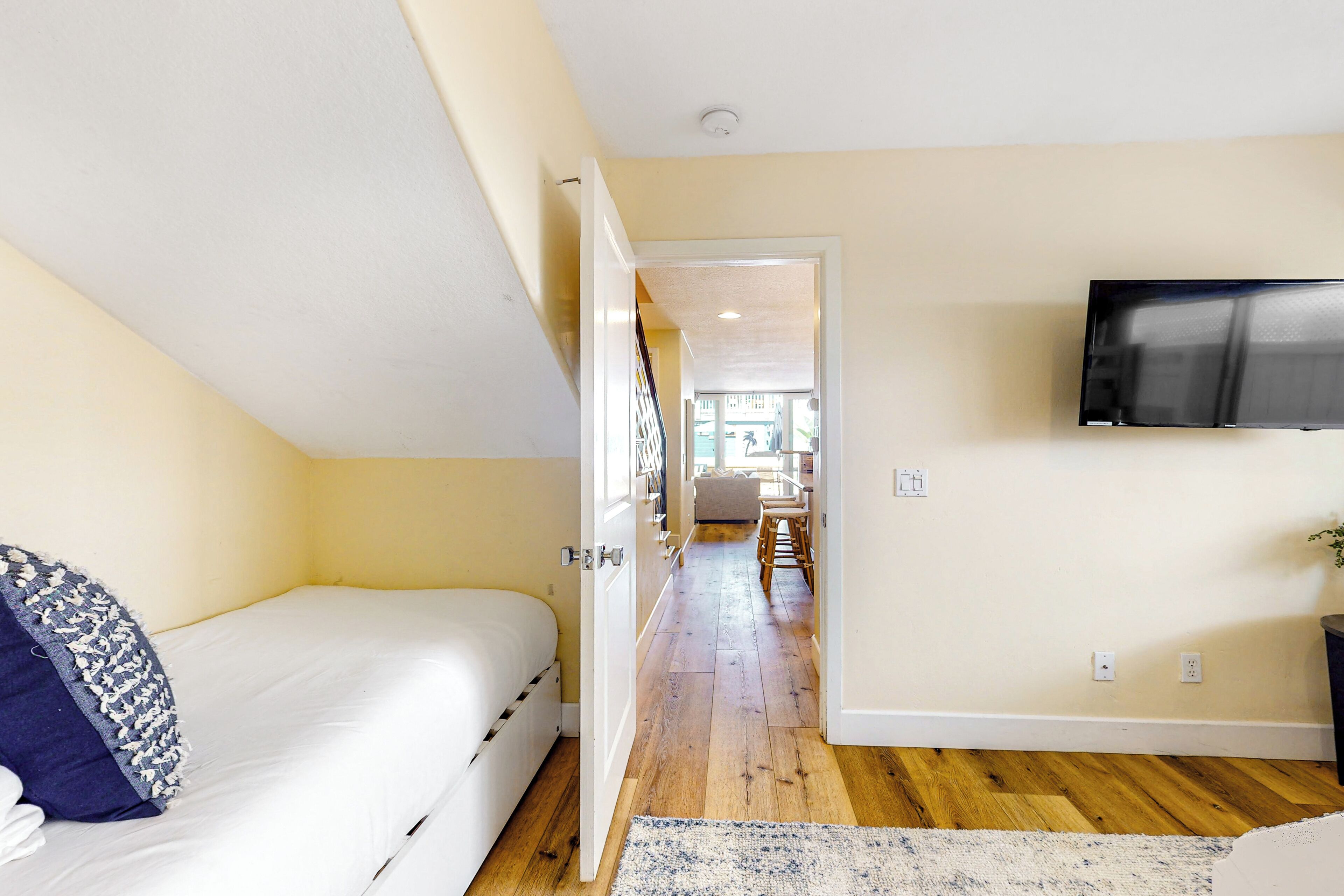Un dormitorio con una cama, un televisor en la pared y suelo de madera.