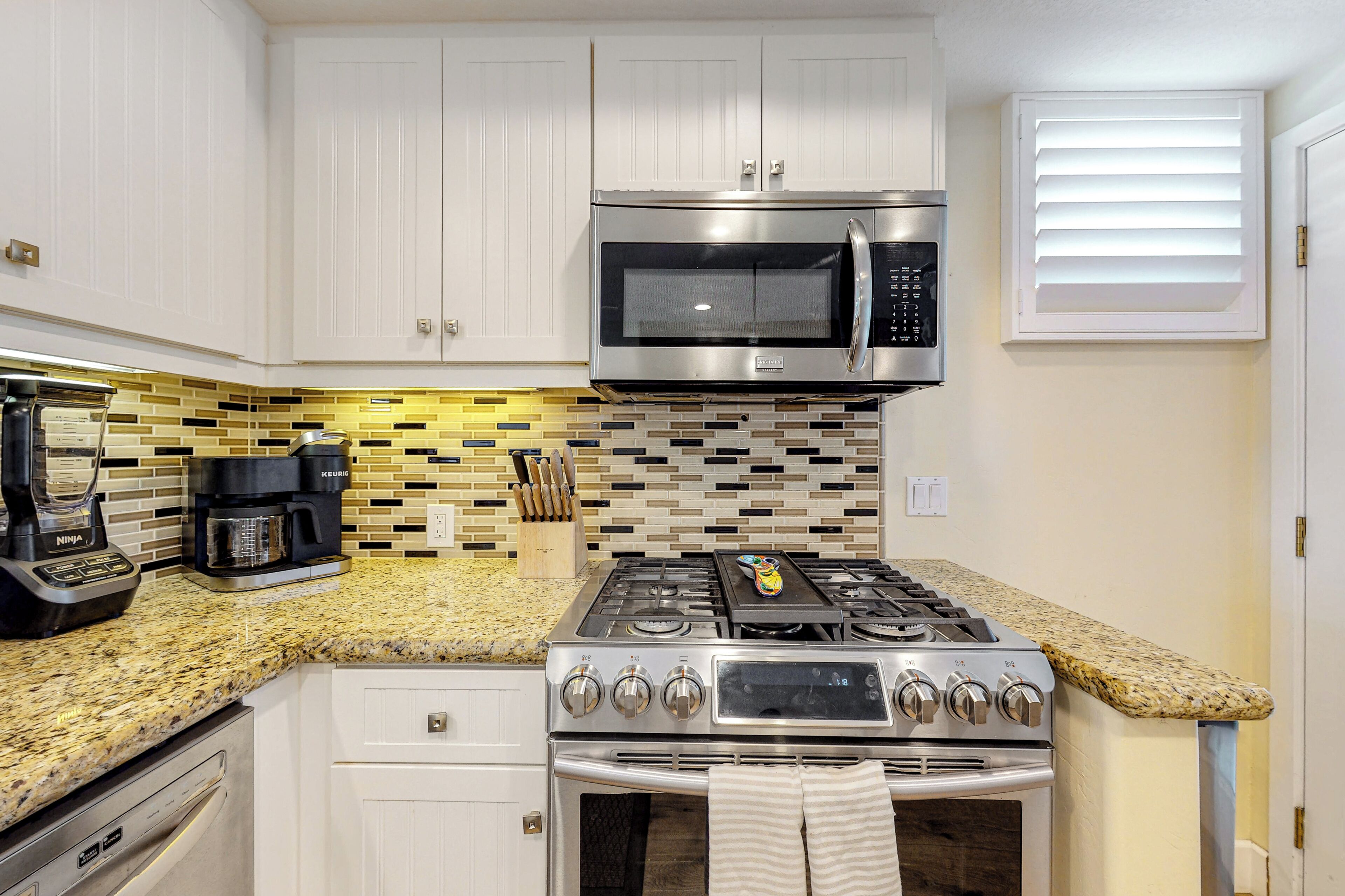 A kitchen with white cabinets, a stainless steel microwave, a gas stove, and a coffee maker.