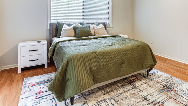 Een slaapkamer met een bed, nachtkastje en een raam met zonwering.