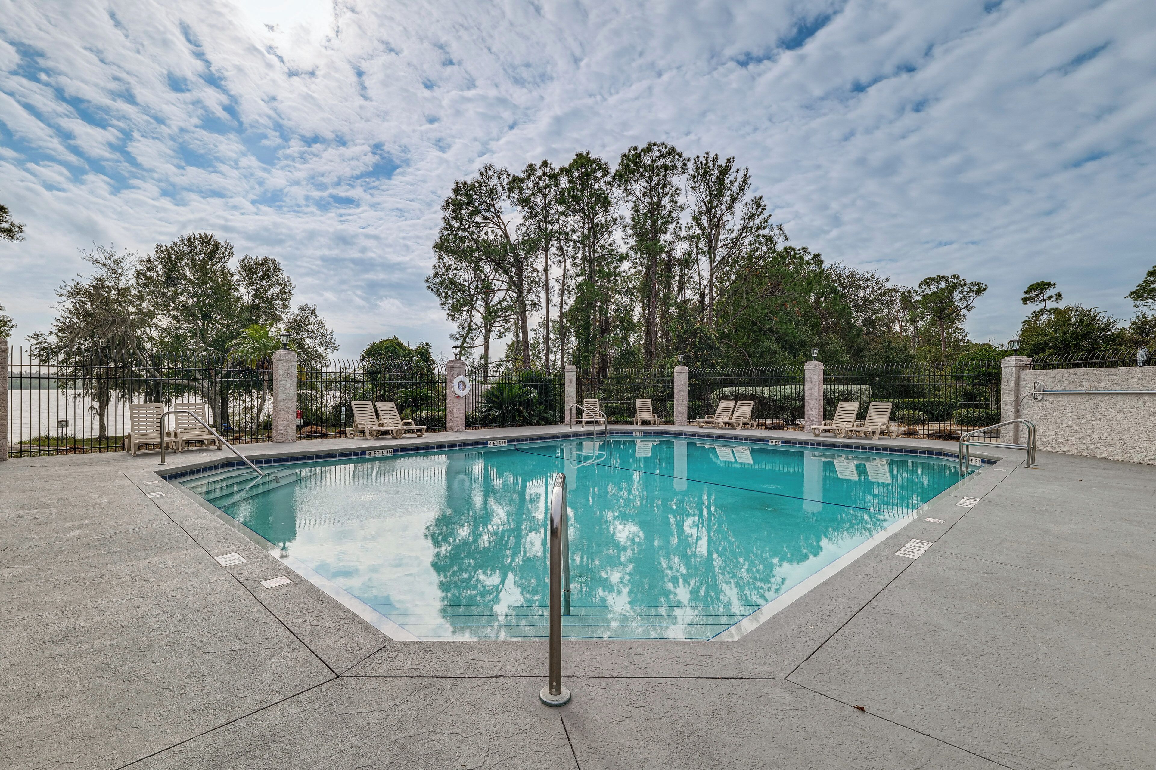 A swimming pool with a metal railing, surrounded by lounge chairs and trees.