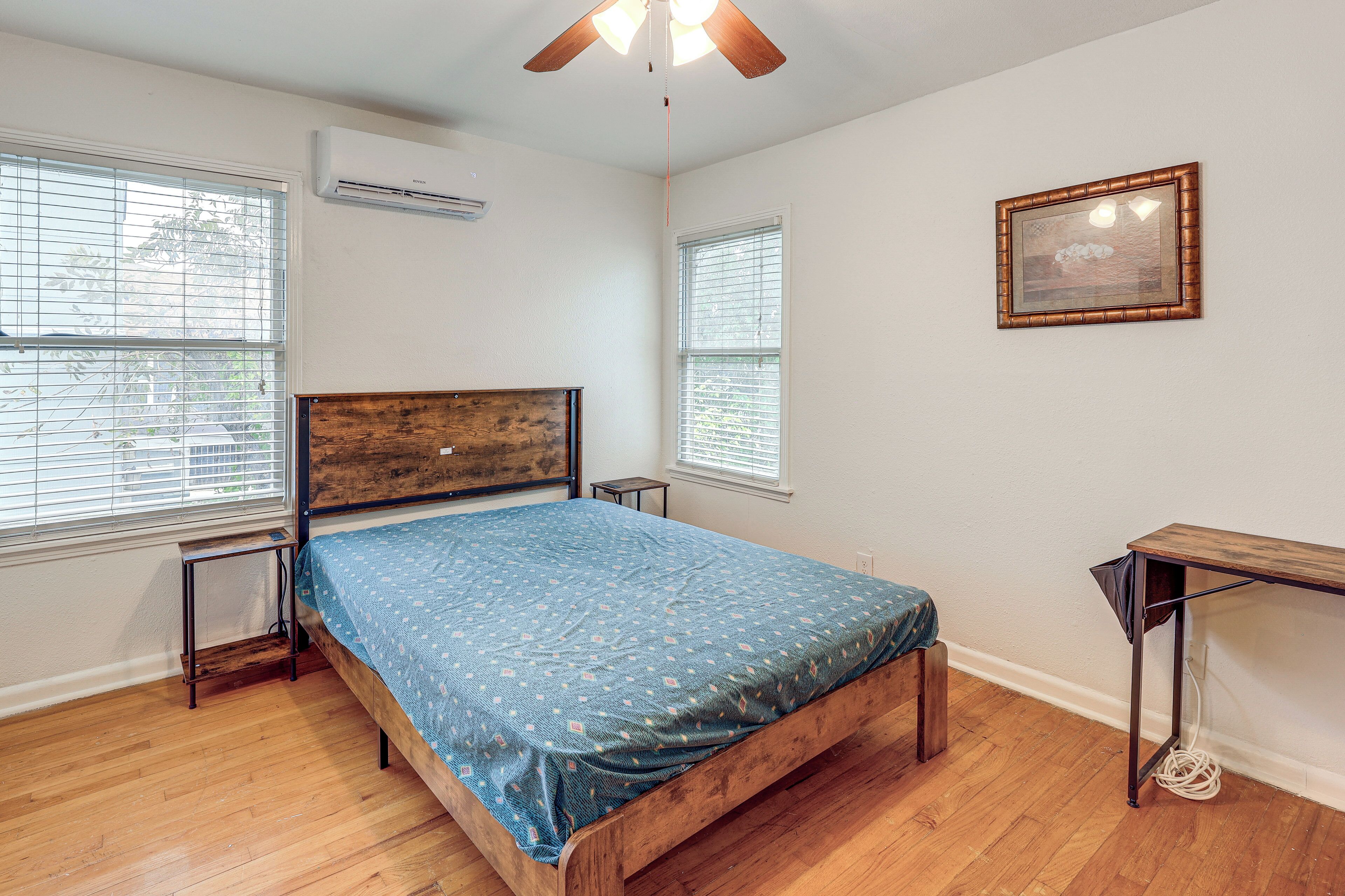 A bedroom with a wooden bed, a small bedside table, a desk, and a ceiling fan.