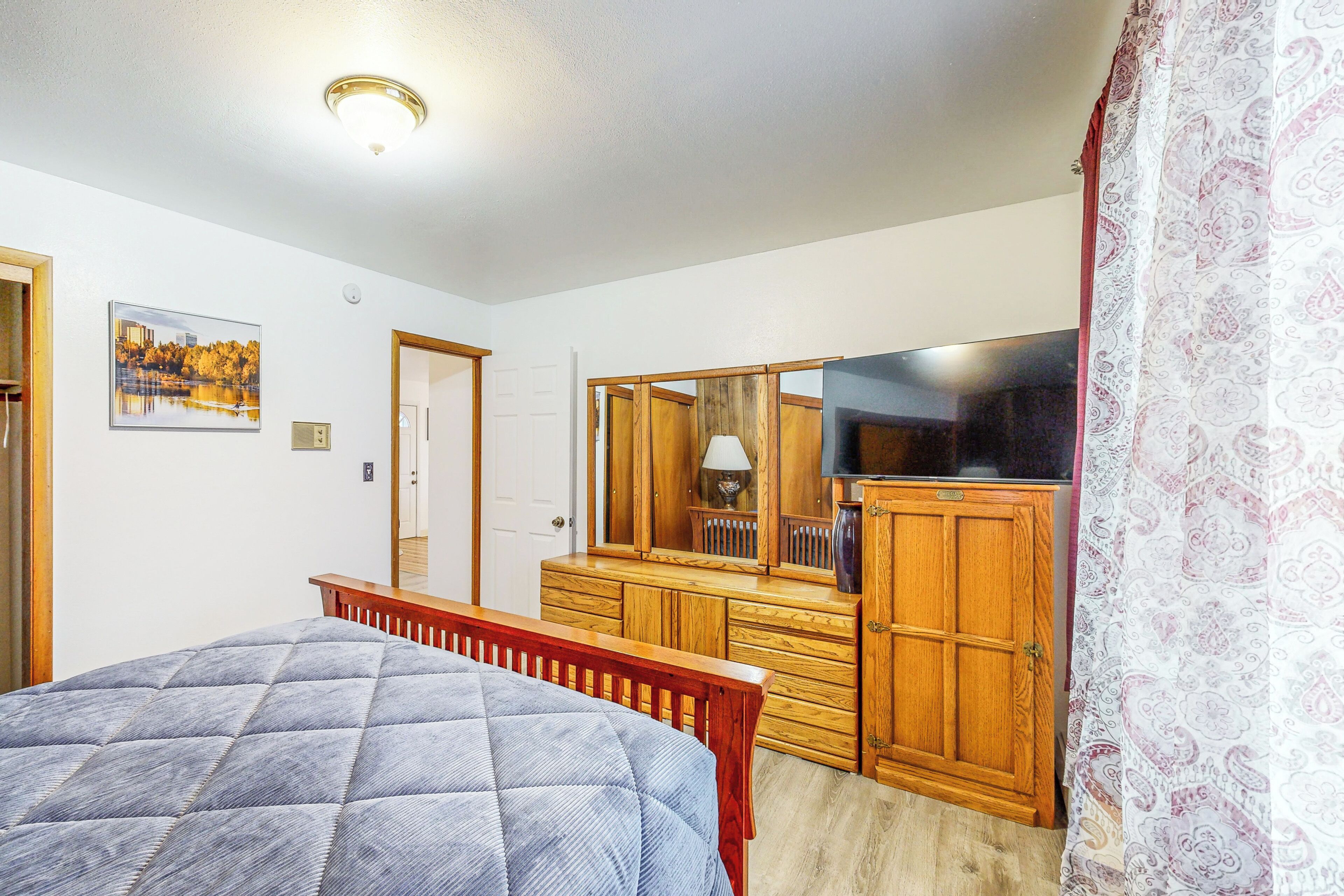 A bedroom with a bed, wooden dresser, mirror, and a painting on the wall.