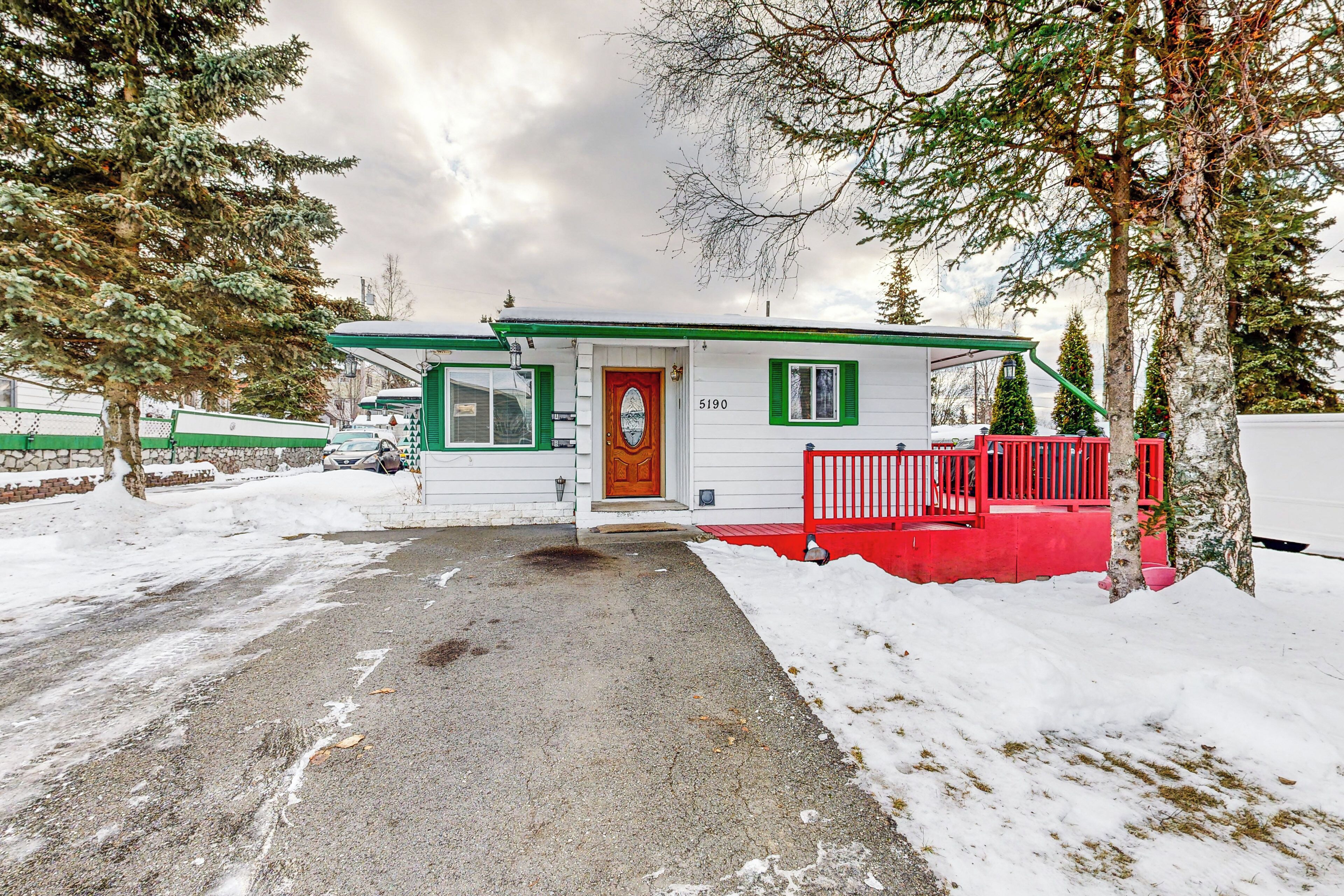 A small, single-story building with a green door and white walls, surrounded by snow and trees.