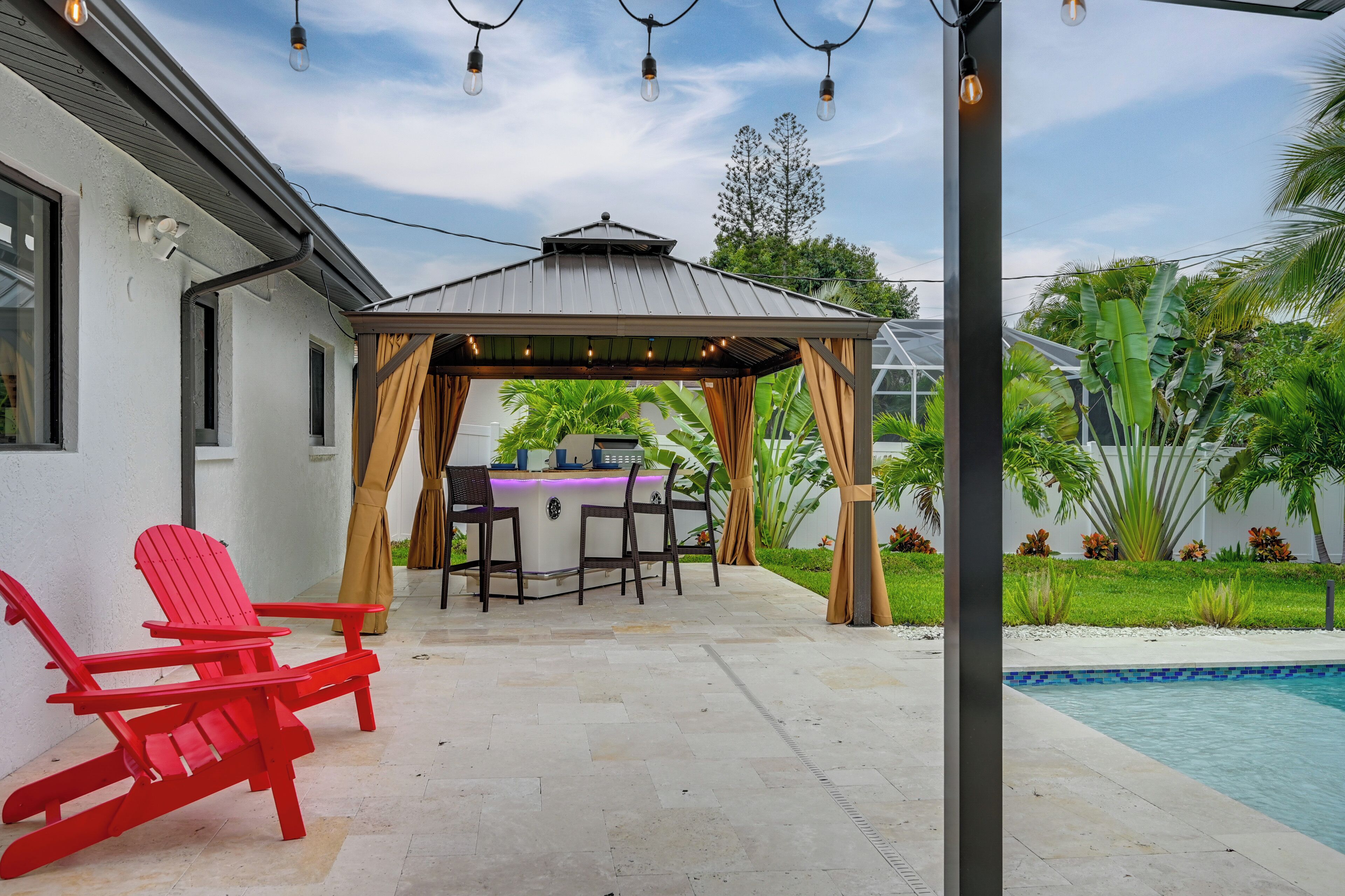 En overdækket patio med swimmingpool, udendørs møbler og en pergola med lyskæder.