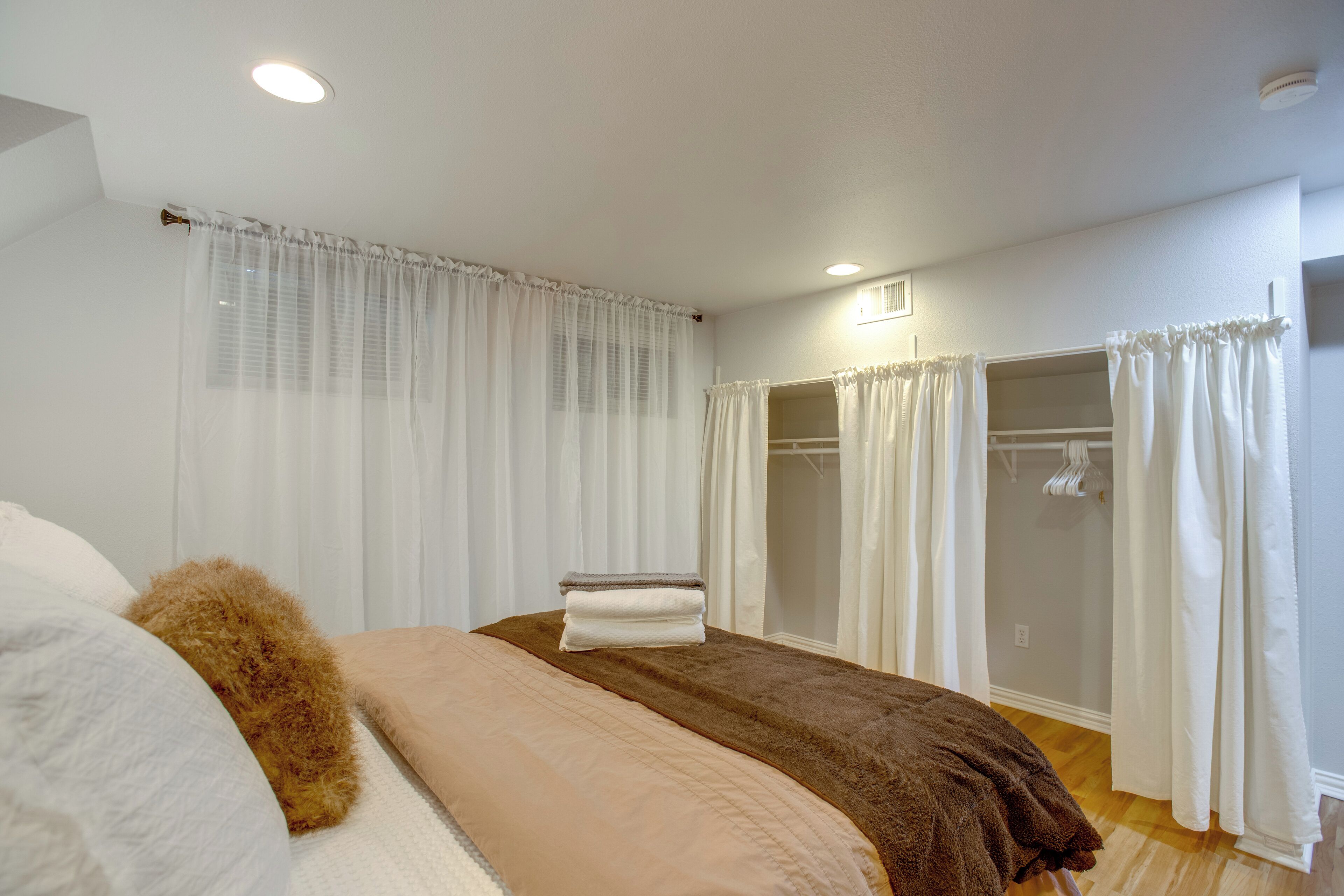 A bedroom with a bed, a wooden floor, a closet with a mirror, and a window with curtains.