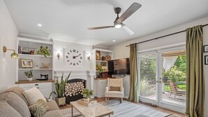 Een woonkamer met een bank, salontafel en een open haard. Er hangt een klok aan de muur en er is een plafondventilator.