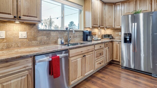 A modern kitchen with wooden cabinets, a stainless steel refrigerator, a built-in dishwasher, and a window providing natural light. - Denver Home w/ Patio Near City Park & Cherry Creek (Denver)
