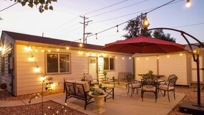 A house with a patio area featuring outdoor furniture, string lights, and a red umbrella. - Denver Home w/ Patio Near City Park & Cherry Creek (Denver)