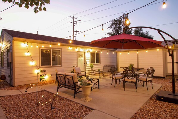 A house with a patio area featuring outdoor furniture, string lights, and a red umbrella. - Denver Home w/ Patio Near City Park & Cherry Creek (Denver)