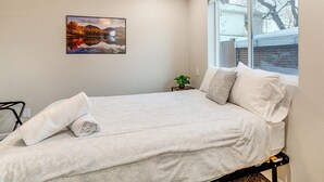 A bedroom with a bed, pillows, a rolled towel, a nightstand with a plant, and a painting on the wall. - Denver Home w/ Patio Near City Park & Cherry Creek (Denver)