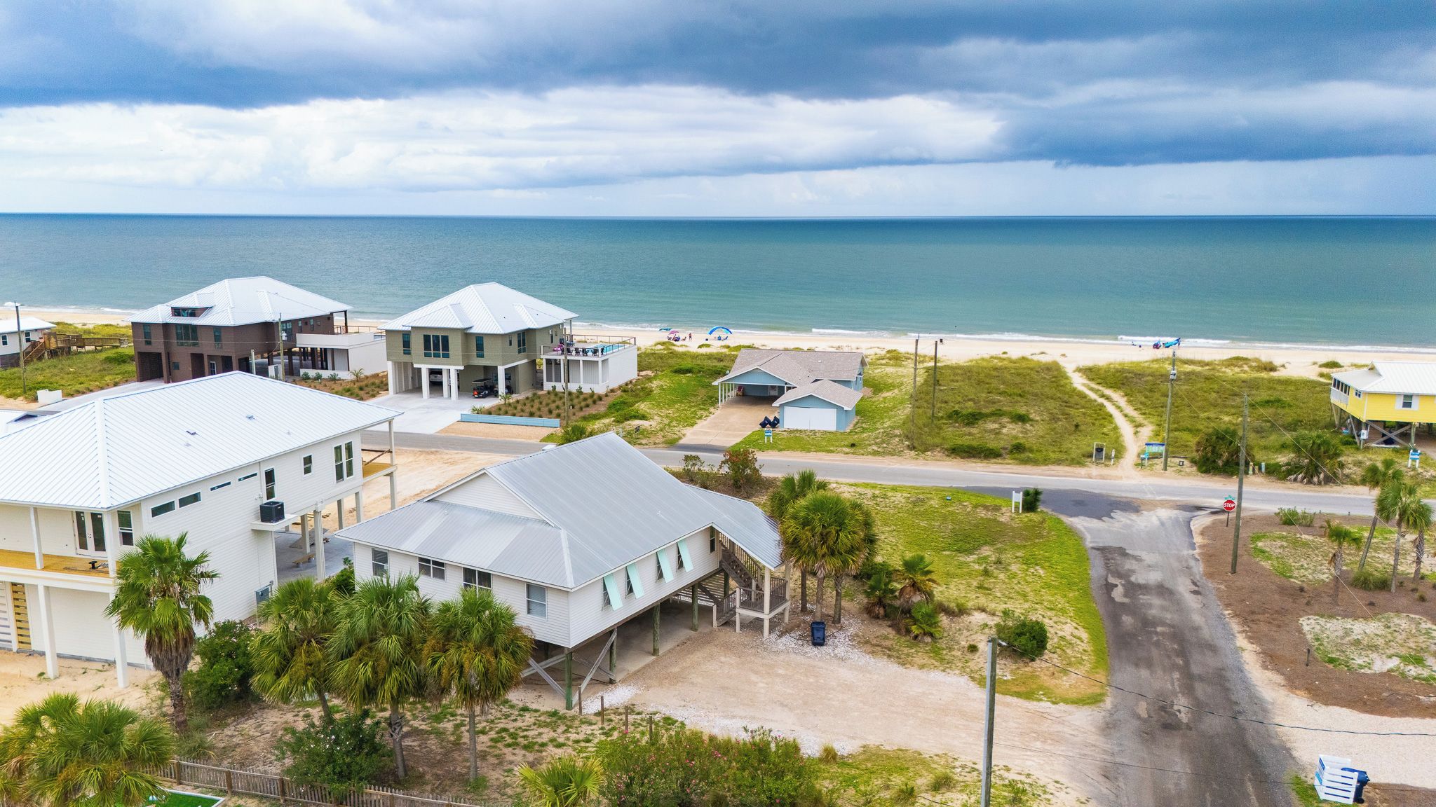 A coastal residential area with houses near the beach, a clear sky, and a road leading to the beach.