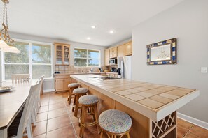 A modern kitchen with a large island, wooden cabinets, and a dining area with a bench and stools. - ENJOY THE WONDERFUL natural daylight in this comfortable home (St. George Island)