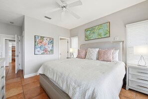 Una camera da letto con un letto grande, una ventola a soffitto, un comodino e un quadro appeso al muro.
