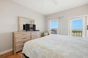 A bedroom with a bed, a dresser, a television, and a view of the outdoors through a door. - ENJOY THE WONDERFUL natural daylight in this comfortable home (St. George Island)